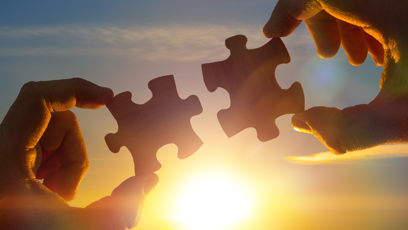 two hands connect the puzzle details, against the sky of the sun.